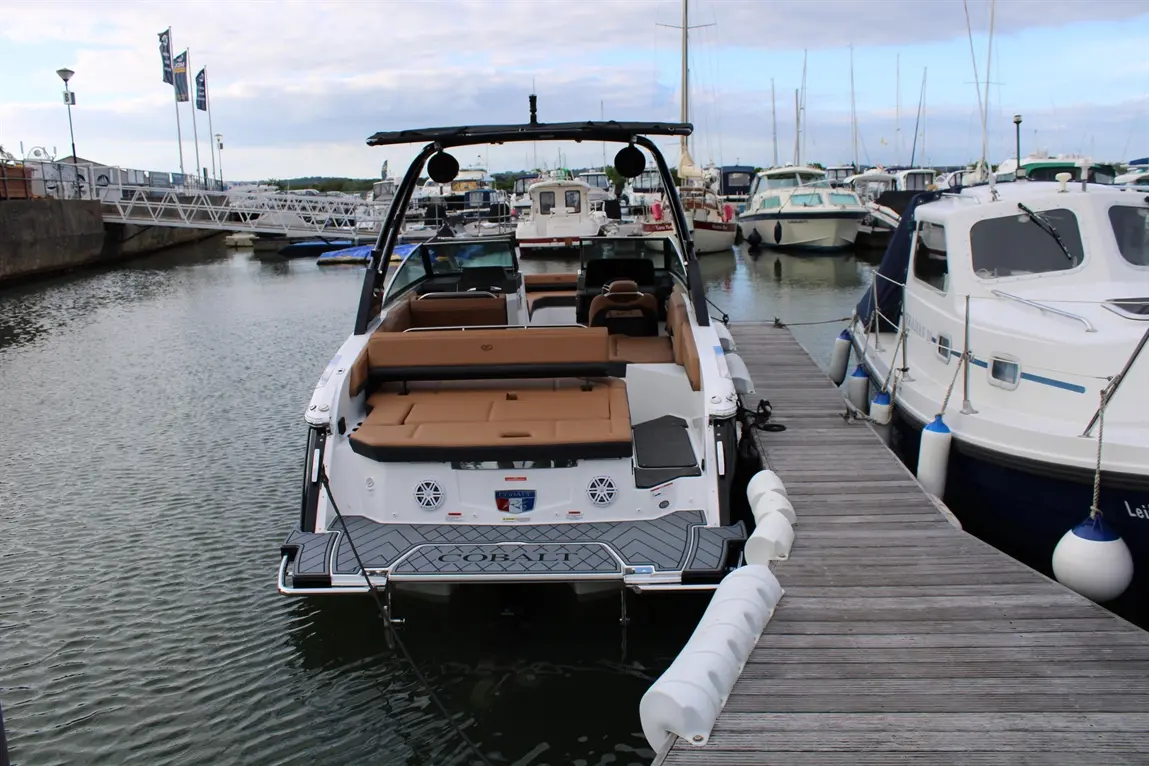 A Cobalt boat docked at a marina, featuring tan seating, surrounded by various other boats and a calm waterway.